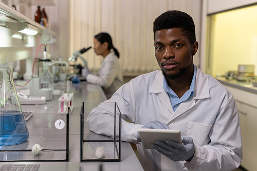 African young scientist looking at camera while working on digital tablet and examining two kinds of mice during scientific experiment