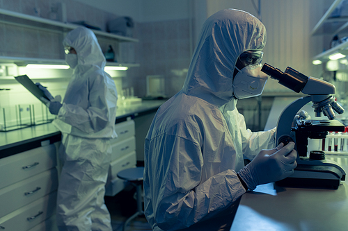People in protective workwear working in the laboratory and examining samples through the microscope