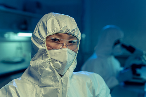 Portrait of Asian young chemist in protective workwear  and glasses looking at camera while working in the laboratory