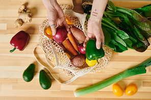 A hand of woman taking fresh vegetables out of shopping bag on wooden kitchen table