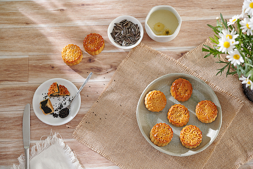 Delicious mooncakes with black sesame filling and cup of herbal tea on wooden table