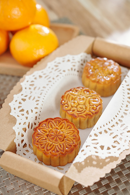 Box of glazed mooncakes decorated with lacy napkin on table prepared for Asian mid autumn festival
