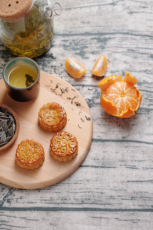 Wooden board with moon cakes, cup of herbal tea and pilled tangerine on wooden table