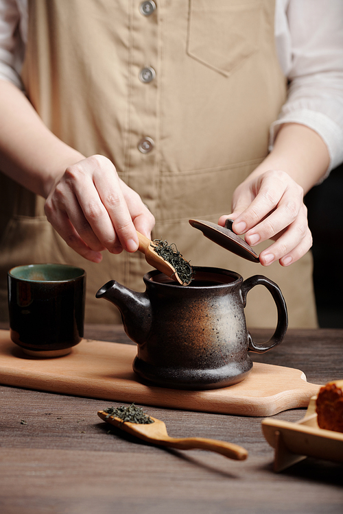 Hands of man steeping tea in ceramic pot at kitchen table