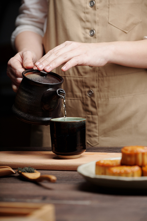 Close-up image of person pouring hot green tea in ceramic cup on wooden table