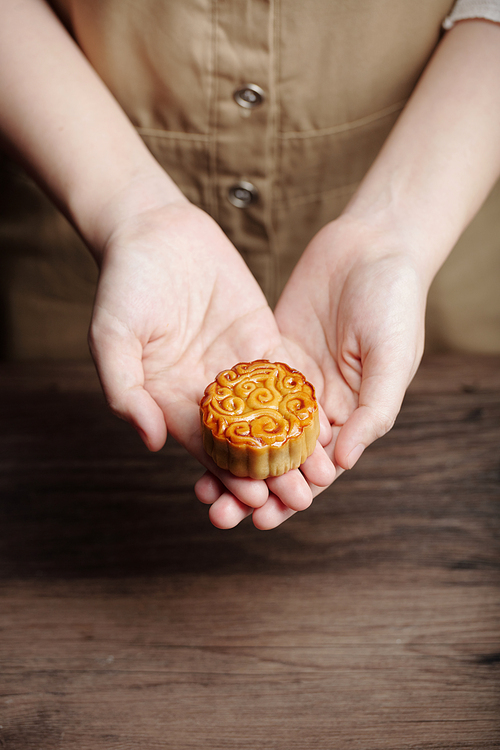 Hands of hospitable woman offering glazed mooncake as a present for mid autumn festival