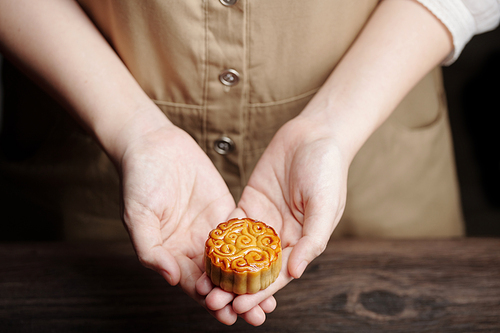 Close-up image of young woman giving small mooncake glazed with eggwash
