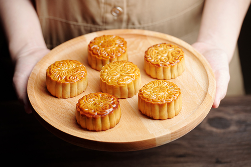 Person offering wooden tray with beautiful various mooncakes prepared for mid autumn festival