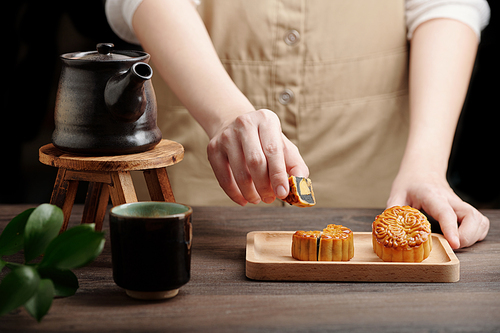 Close-up image of woman serving mooncakes with black sesame filling and hot tea for mid fall celebration