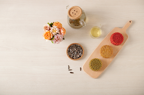 Cutting board with colorful mooncakes, pot of green tea and sunflower seeds on table, view from the top