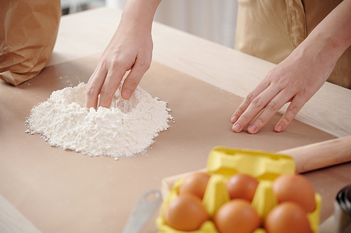 Hands of woman creating a well in the center of the flour to add egg and mix dough