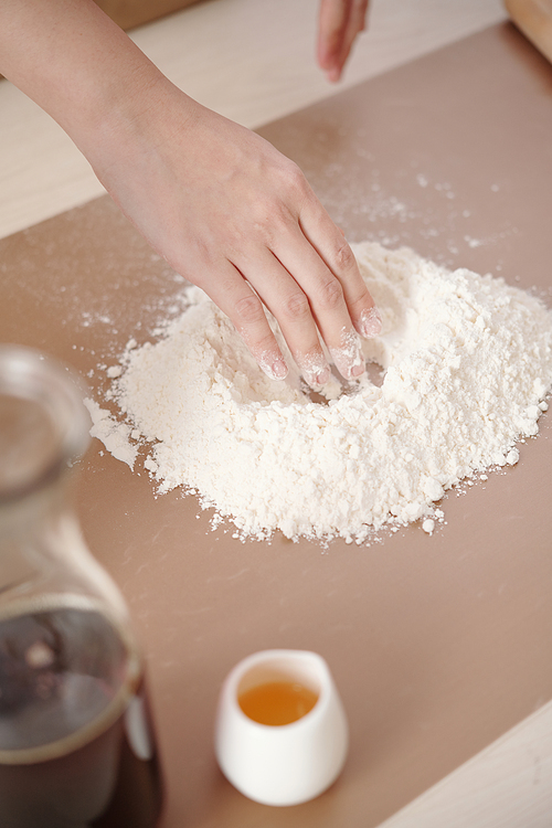 Close-up image of woman adding egg yolk to sifted white flour when making dough for mooncakes