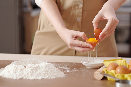 Hands of young woman separating egg yolks from egg whites when making dough