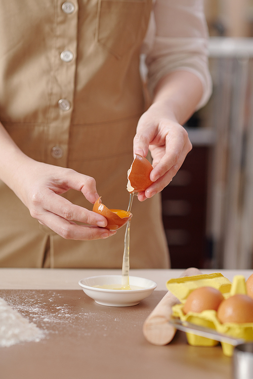 Process of young woman separating egg yolk from white when making dough for pastry