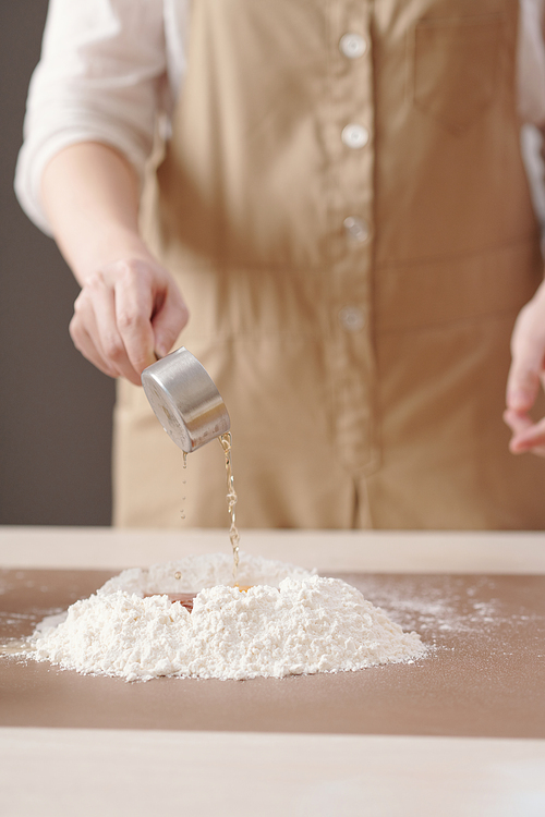 Person pouring Lye water in pile of flour to mix mooncake dough ingredients