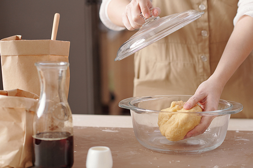 Cropped image of young woman putting dough in glass saucepan to let the dough relax