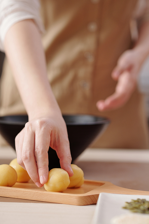 Close-up image of woman putting dough balls she made at home on wooden board