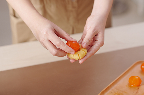 Close-up image of woman wrapping salted egg yolk in dough when making mooncakes at home for traditional celebration
