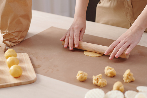 Close-up image of woman rolling out piece of dough when making mooncakes at home