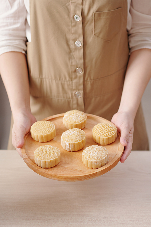 Hands of woman holding round wooden tray with decorated raw mooncakes ready for baking
