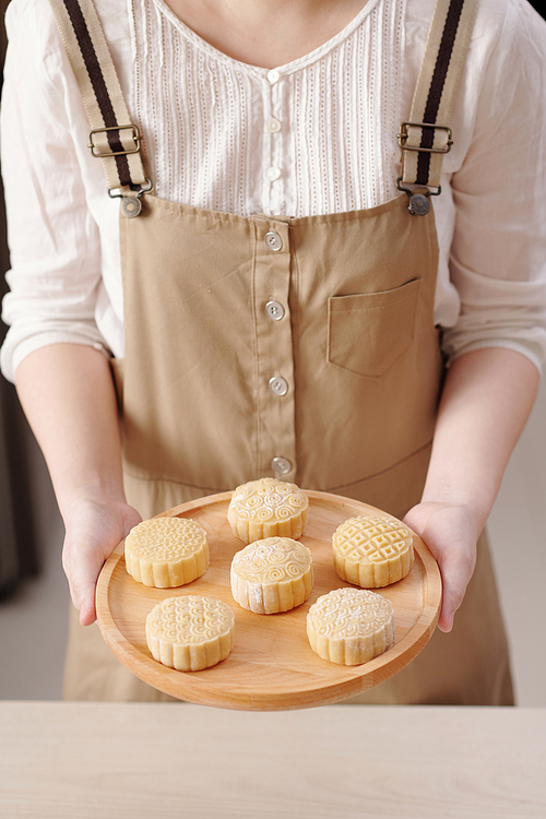 Cropped image of woman holding wooden tray with mooncakes ready to be baked in oven