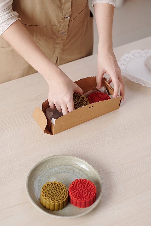 Hands of woman packing delicious mooncakes in box as a gift for traditional mid autumn festival