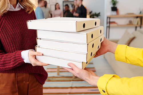 Young smiling blond female in smart casualwear taking stack of packed square carton boxes with pizza from hands of male courier in uniform