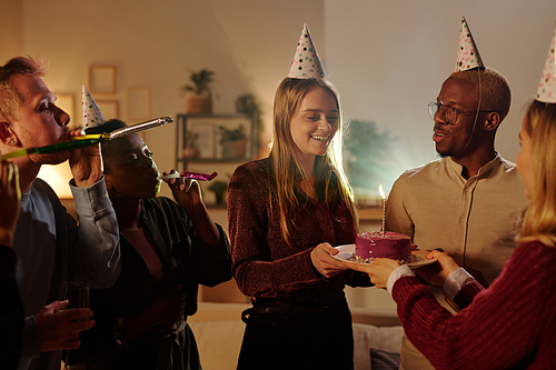 Happy young intercultural friends congratulating gorgeous blond girl on her birthday while pretty female passing her plate with delicious cake