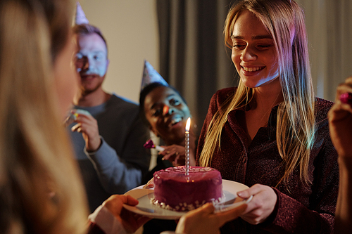 Happy young intercultural friends congratulating smiling girl on her birthday while one of females passing her plate with delicious cake