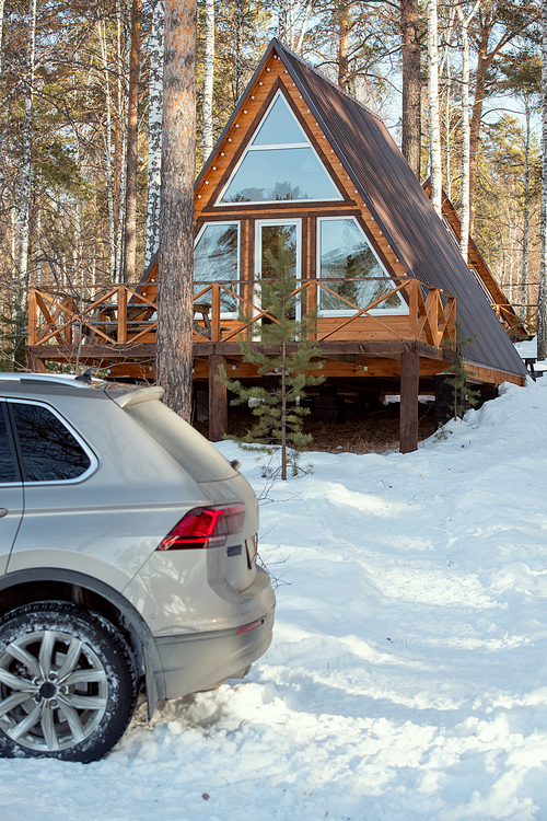 Back of the car of silver color standing in snowdrift in front of camera on background of country house in the forest on winter weekend