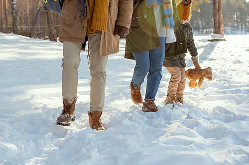 Low section of mother and little daughter in warm winterwear having fun in snowdrift on their way to country house, father moving in front of them