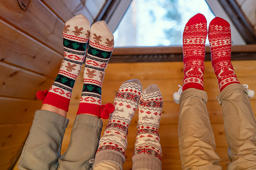 Legs of contemporary restful family of father, mother and little daughter in beige jeans and Christmas socks relaxing inside their country house