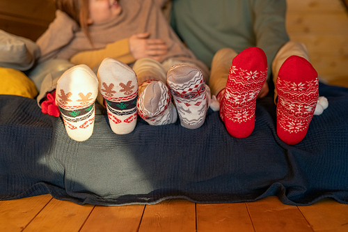 Legs of restful family of father, mother and little daughter in casualwear and Christmas socks relaxing on the floor inside their country house