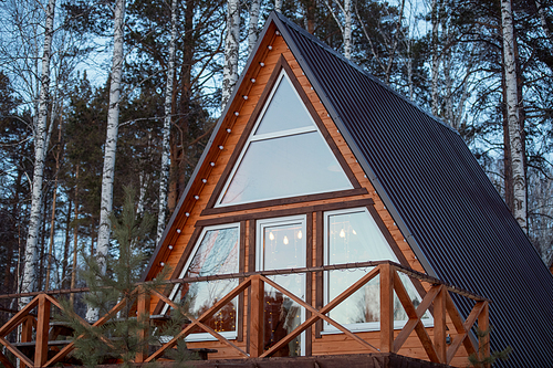 Contemporary new large country house standing in mixed forest in front of camera on background of pine trees and birches growing together