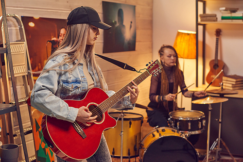 Female musicians playing guitar and drum in modern studio
