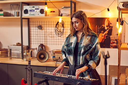 Blond girl playing keyboard in studio of music recording