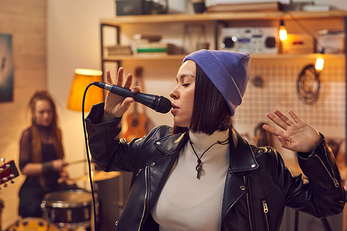 Brunette girl singing in microphone against her friends playing musical instruments