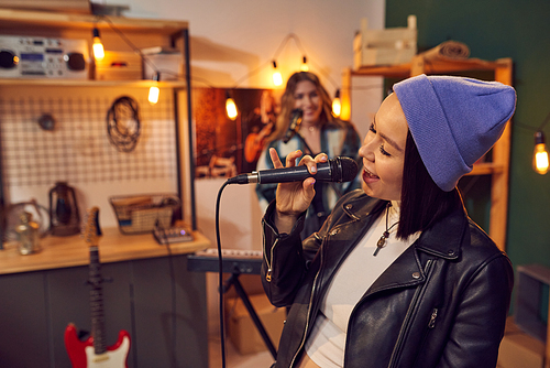 Cheerful young woman with microphone singing against her friend playing keyboard