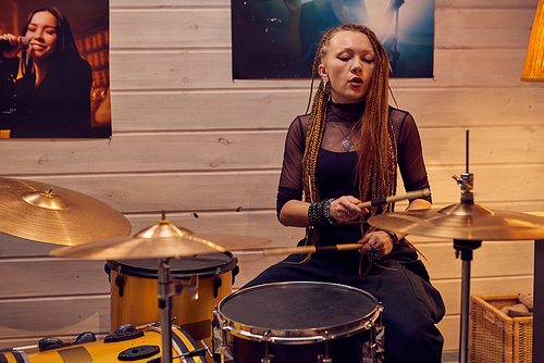 Girl sitting by drum set while recording music in modern studio