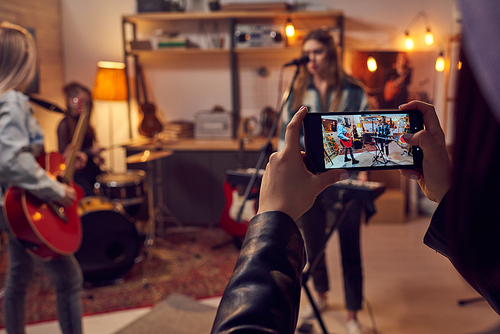 Girls with smartphone taking video of her band playing musical instruments in studio