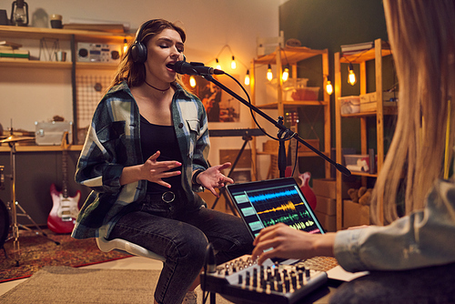 Blond girl singing in microphone while her friend recording new songs