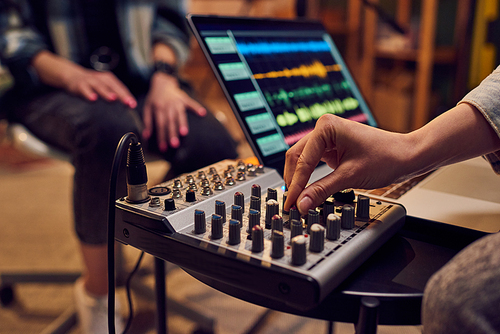 Hand of young female adjusting sound whil.e recording music in studio