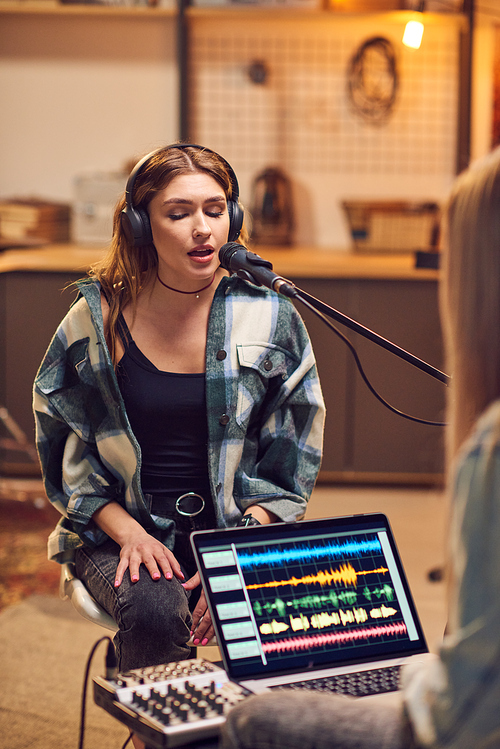 Young female singing in microphone in front of other girl recording her