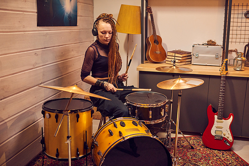 Young female beating drum with drumsticks during repetition in garage