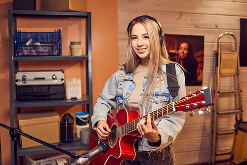 Happy blond girl in denim jacket playing electric guitar