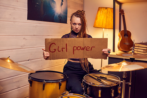 Young female rock musician holding cardboard poster about power of girls