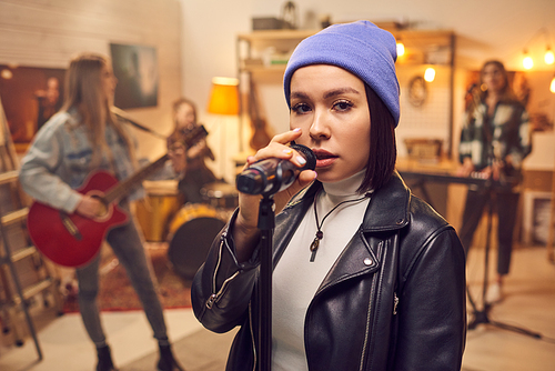 Young female with microphone singing in front of camera with her band on background