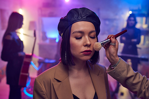 Hand of makeup artist applying powder on face of young woman before recording performance