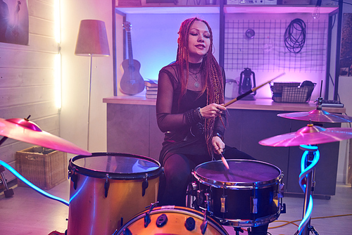 Young female with braids hitting cymbals of drum kit during repetition