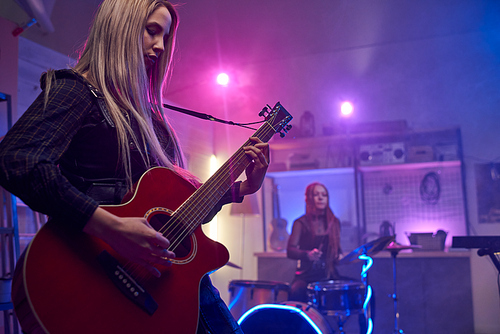 Pretty blond female playing electric guitar during stage performance